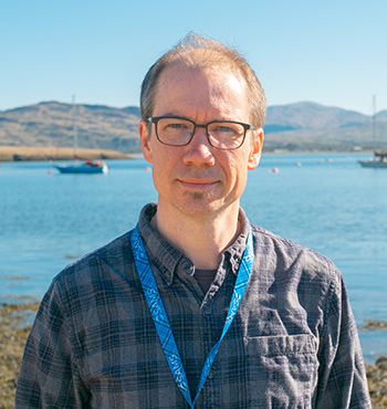 Rob Hall standing on the beach at SAMS with boats and mountains in the background