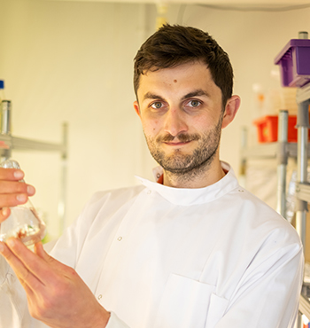 Head and shoulder picture of Rob Grisenthwaite in a white lab coat holding a glass vial in a lab