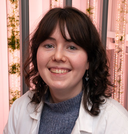 CCAP support scientist Evie Whyte in a lab coat in front of large tubes with growing algae