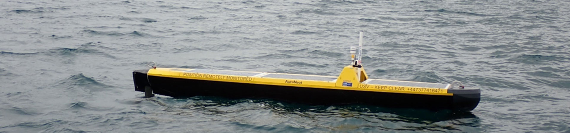 An unstaffed autonomous surface vehicle in the sea en-route to recovering data from a seabed recorder with a castle in the background 