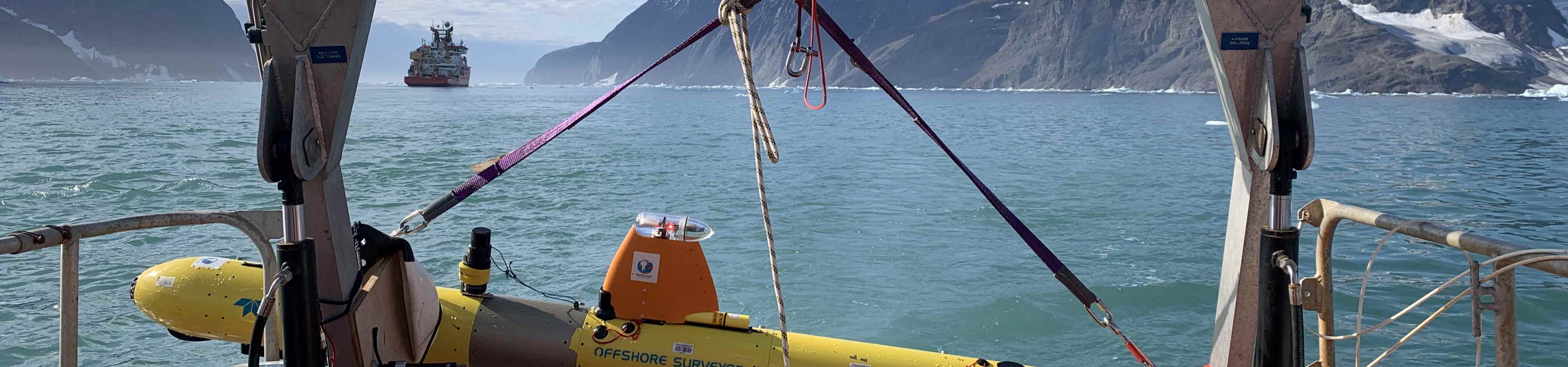 Submersible held in crane over water and with research vessel in background